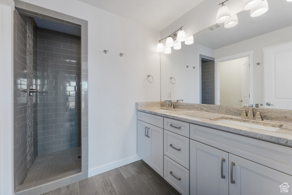 Bathroom with double vanity, visible vents, a tile shower, and a sink