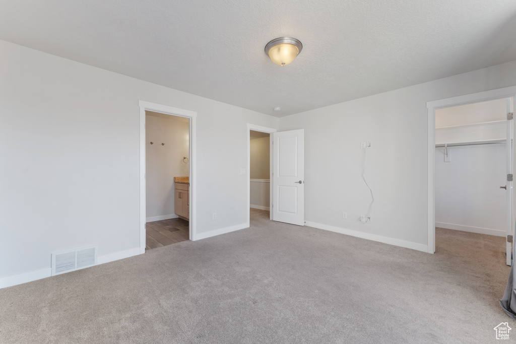 Unfurnished bedroom featuring baseboards, visible vents, carpet, a walk in closet, and a closet