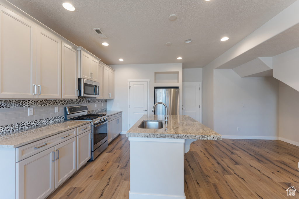 Kitchen featuring tasteful backsplash, visible vents, light wood-style flooring, stainless steel appliances, and a sink