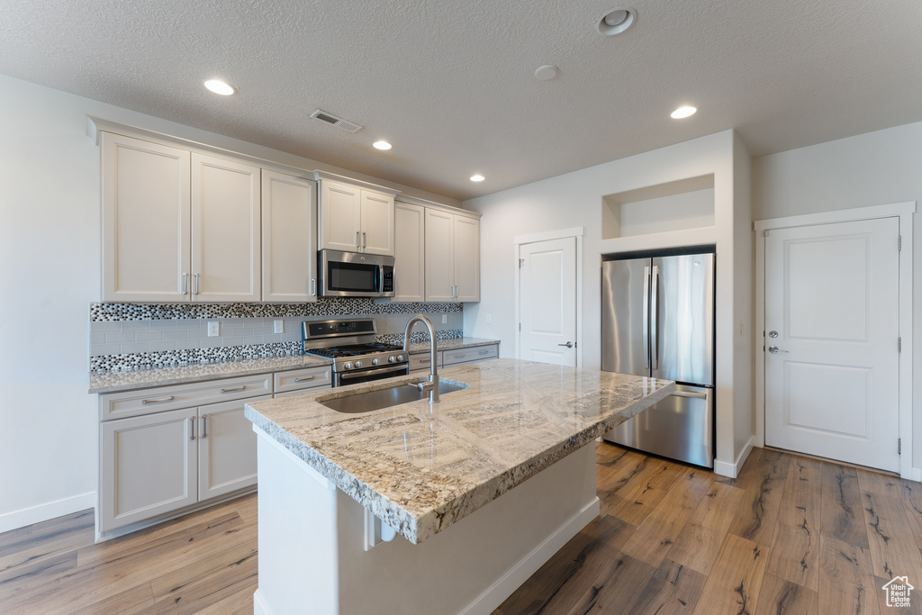 Kitchen featuring stainless steel appliances, a sink, visible vents, light wood-type flooring, and decorative backsplash