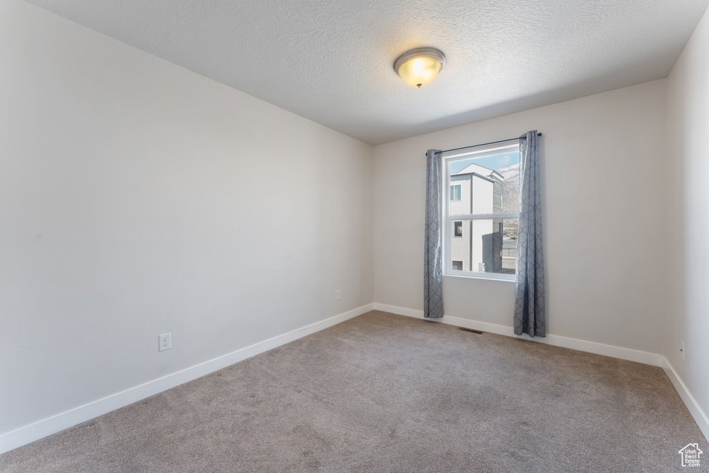 Empty room with carpet, visible vents, a textured ceiling, and baseboards