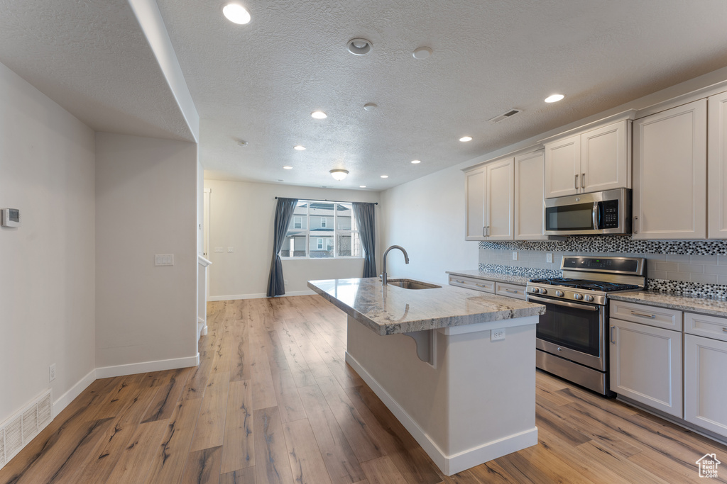 Kitchen with tasteful backsplash, visible vents, stainless steel appliances, light wood-type flooring, and a sink