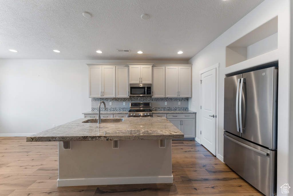 Kitchen with appliances with stainless steel finishes, dark wood-style flooring, a sink, and a kitchen bar