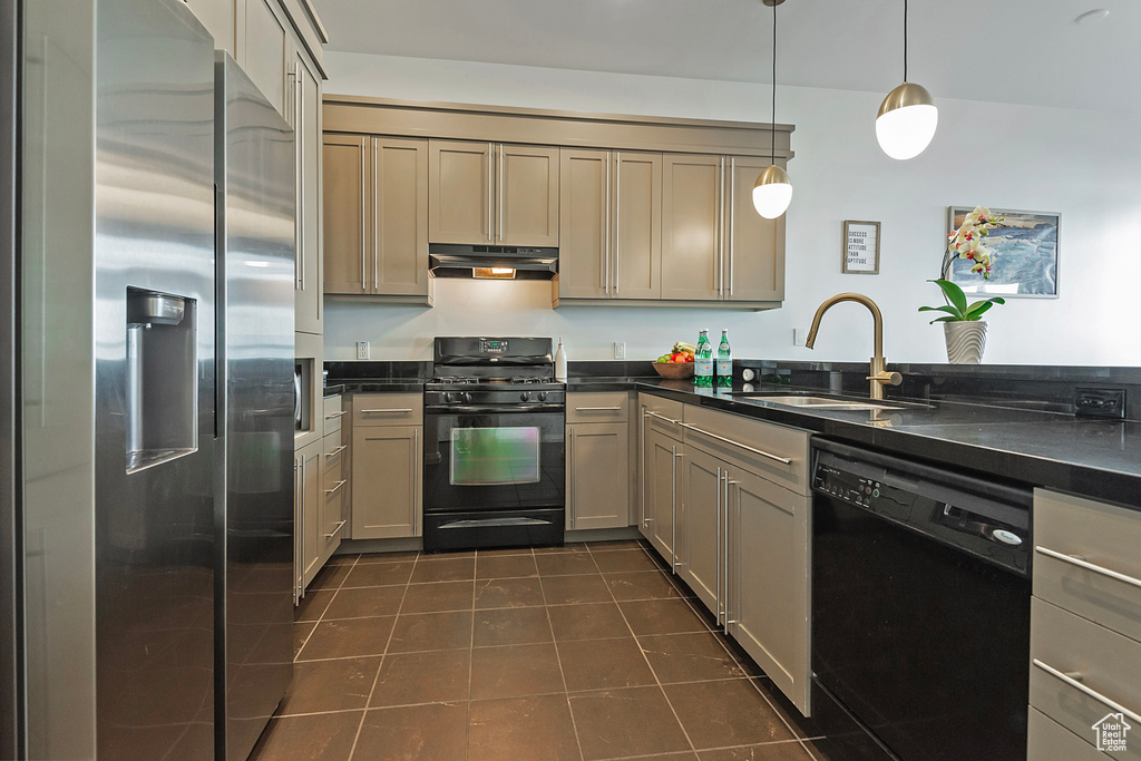 Kitchen featuring dark countertops, under cabinet range hood, black appliances, dark tile patterned floors, and a sink