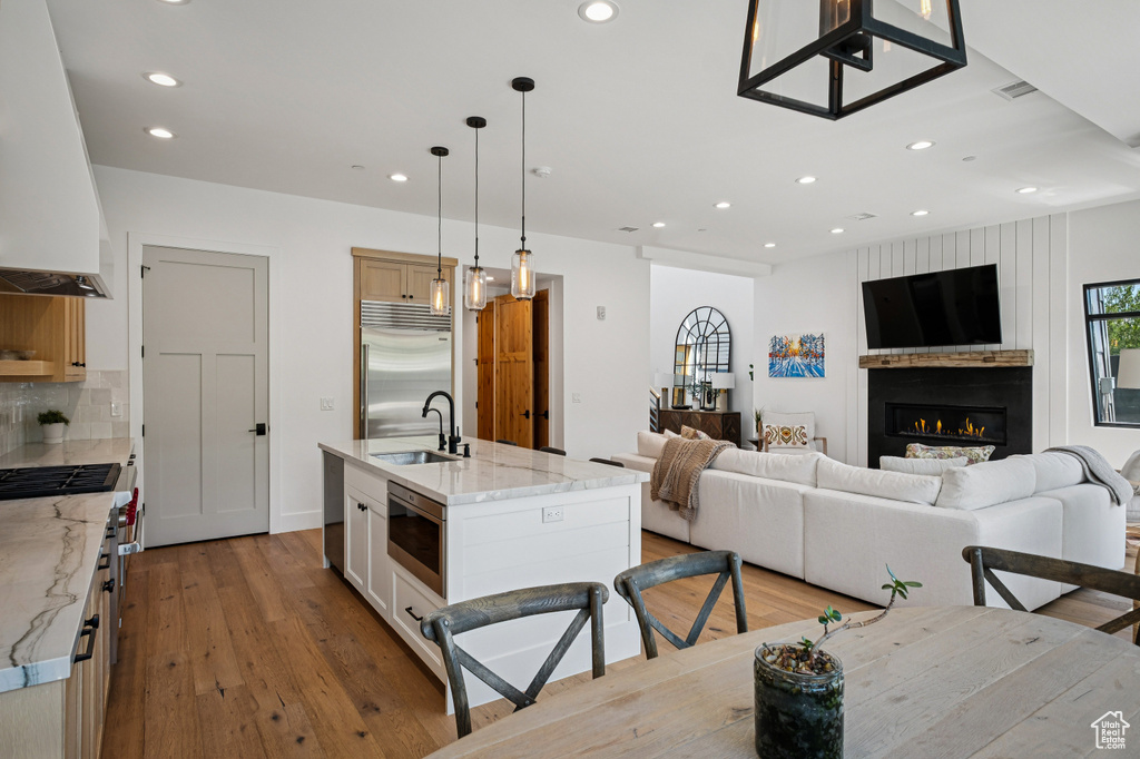 Kitchen with built in appliances, custom range hood, light wood-type flooring, open floor plan, and light stone counters
