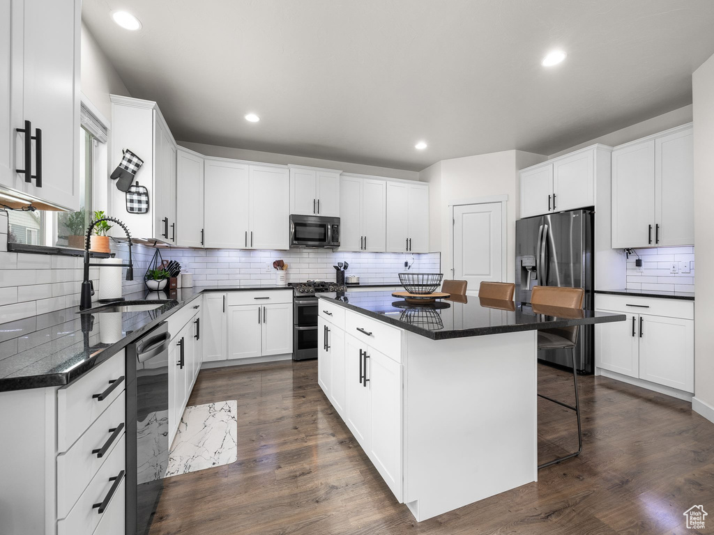 Kitchen with stainless steel appliances, dark countertops, a sink, a kitchen island, and a kitchen bar