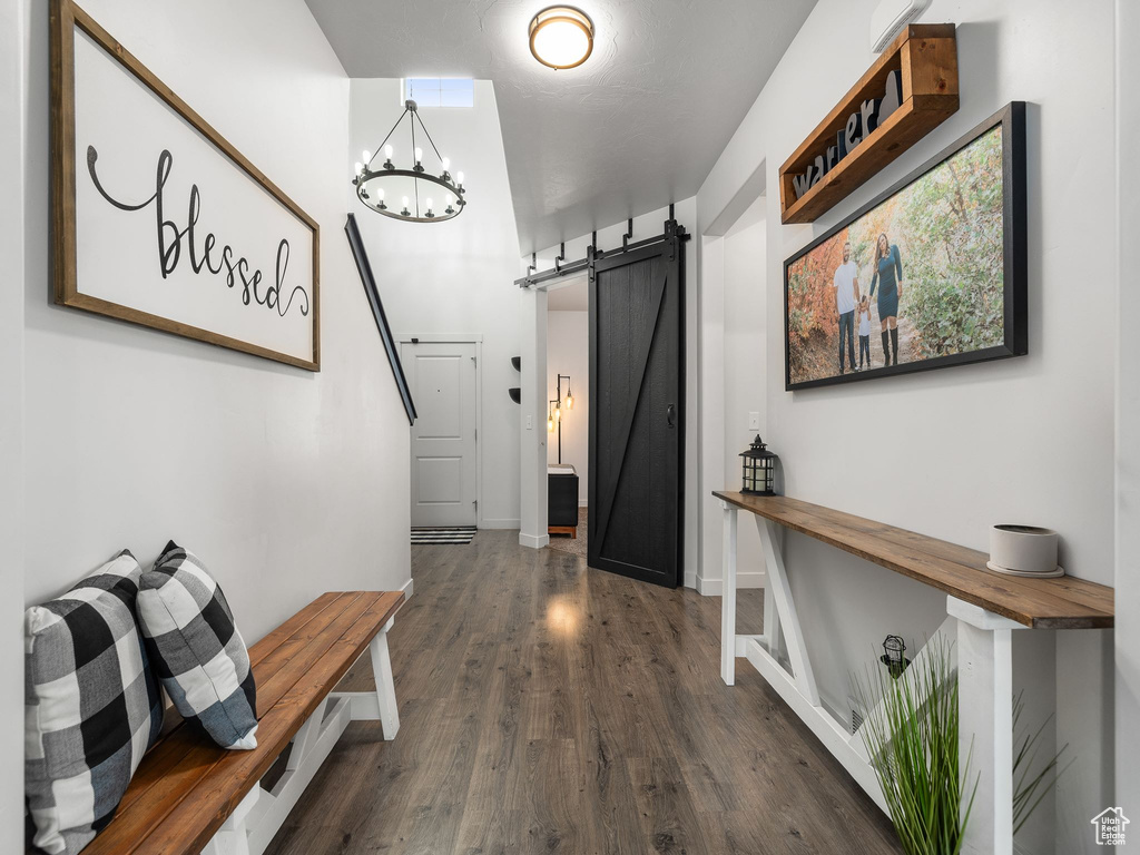 Hallway with dark wood-style floors, a barn door, baseboards, and an inviting chandelier