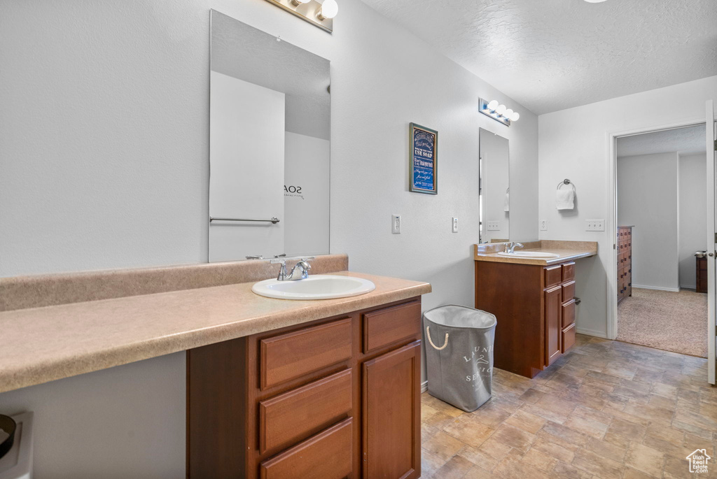 Full bath with a textured ceiling, stone finish floor, two vanities, and a sink