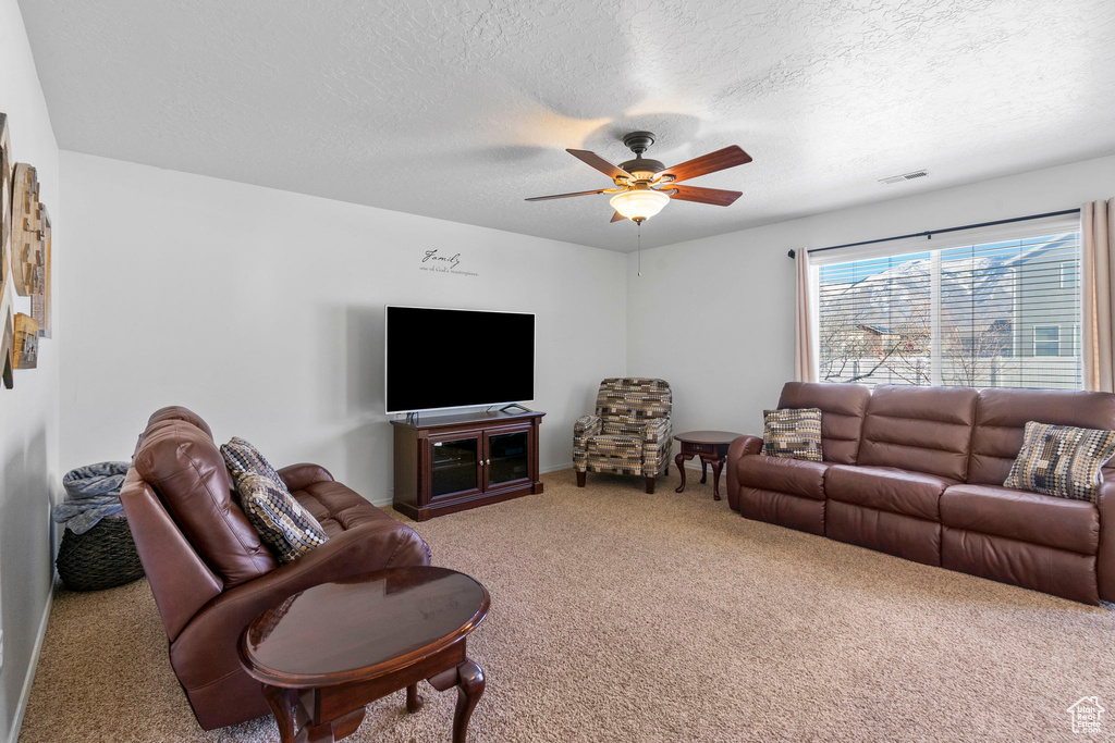 Carpeted living room featuring ceiling fan, visible vents, and a textured ceiling