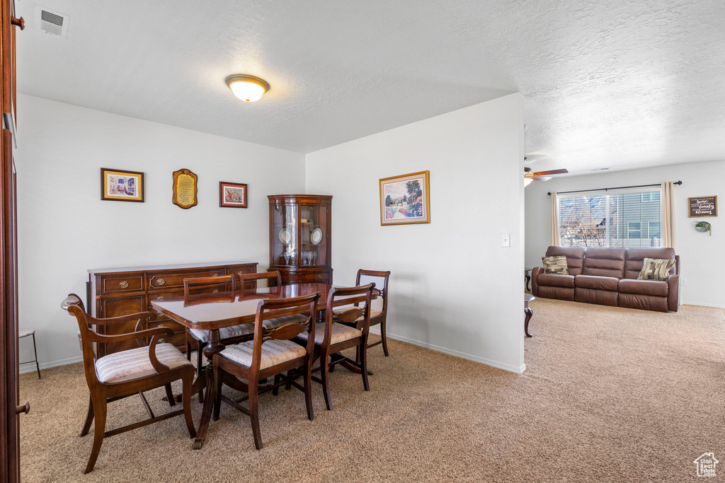 Dining room with light carpet, baseboards, visible vents, a ceiling fan, and a textured ceiling