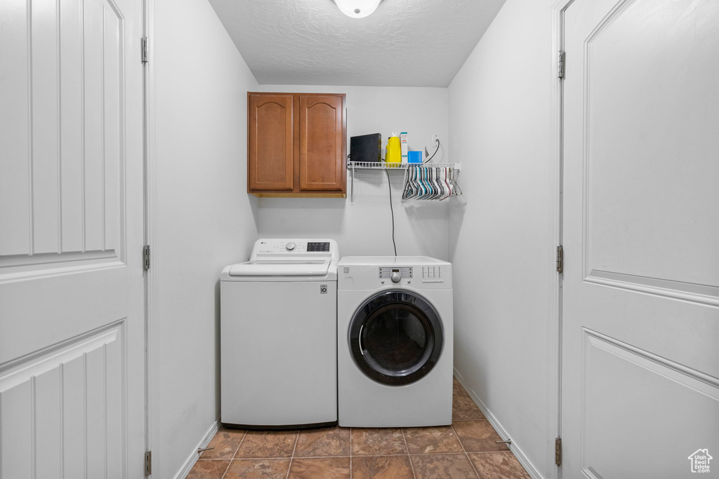 Laundry area with baseboards, cabinet space, a textured ceiling, and washing machine and clothes dryer