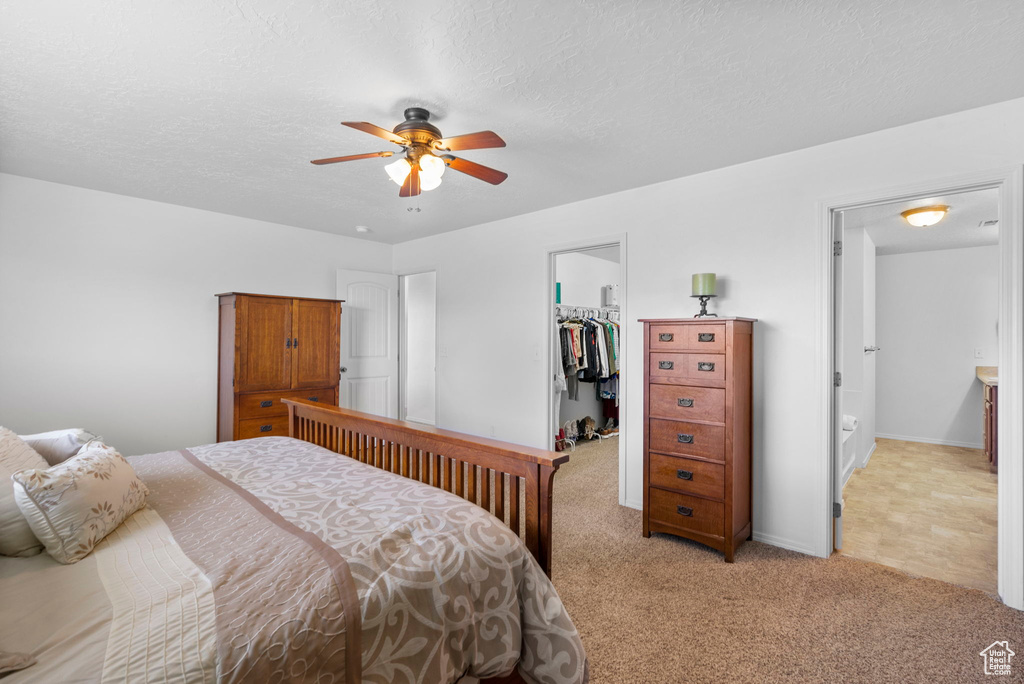 Bedroom featuring a textured ceiling, light colored carpet, a ceiling fan, a closet, and a walk in closet