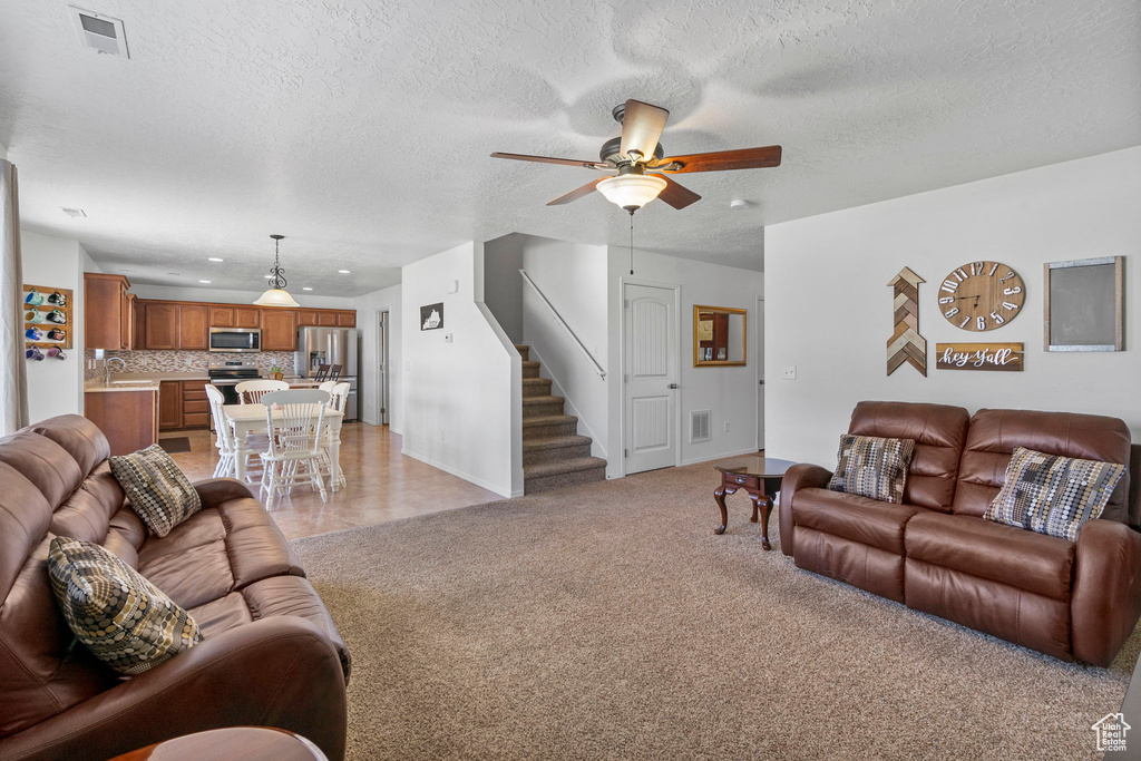 Living room with visible vents, stairway, ceiling fan, and light colored carpet