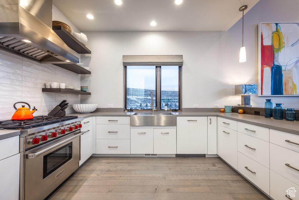 Kitchen featuring luxury range, island range hood, white cabinets, light wood finished floors, and decorative backsplash