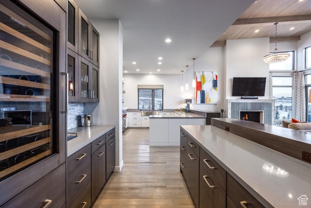 Kitchen with wine cooler, light wood-style flooring, a tiled fireplace, glass insert cabinets, and tasteful backsplash