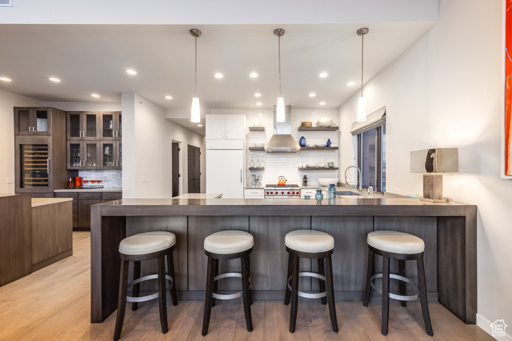 Kitchen with beverage cooler, island exhaust hood, tasteful backsplash, a breakfast bar area, and light wood-style floors