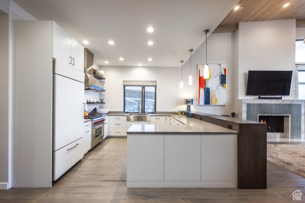 Kitchen with freestanding refrigerator, wall chimney range hood, high end stainless steel range oven, a peninsula, and open shelves