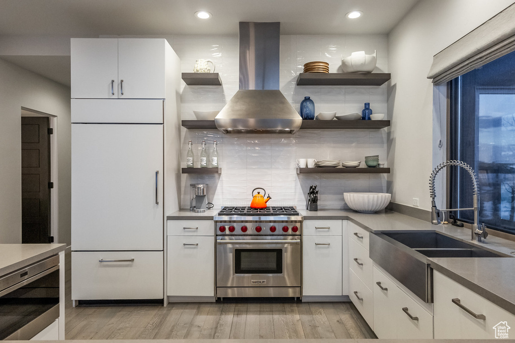 Kitchen featuring built in appliances, island range hood, open shelves, light wood-type flooring, and white cabinetry