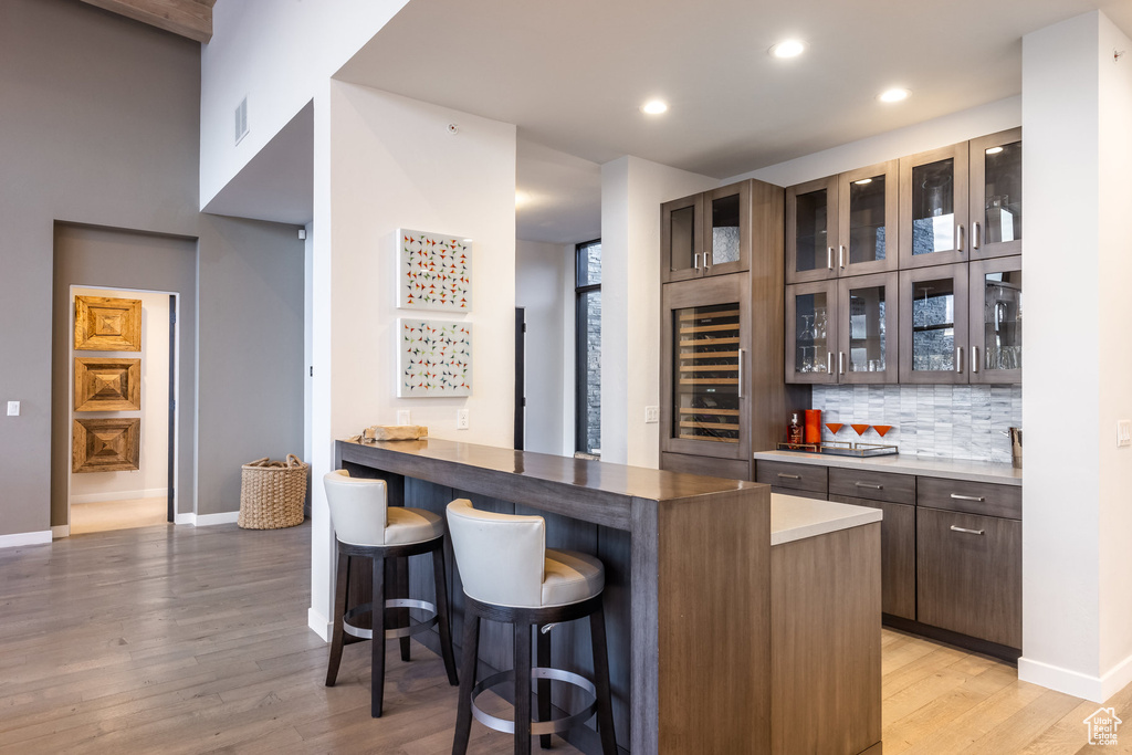 Indoor bar featuring wine cooler, light wood-style floors, decorative backsplash, and recessed lighting