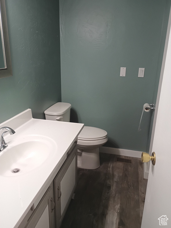Half bathroom with visible vents, toilet, vanity, wood finished floors, and baseboards