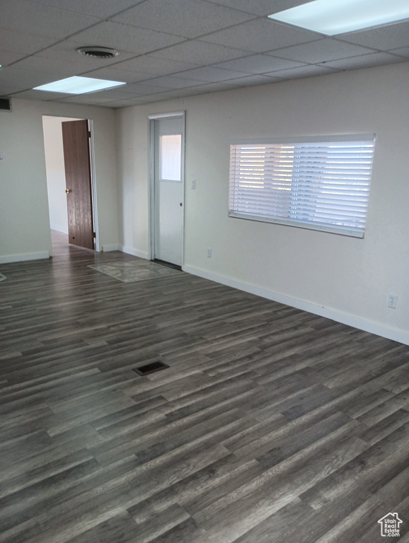 Empty room with dark wood-style floors, a drop ceiling, visible vents, and baseboards