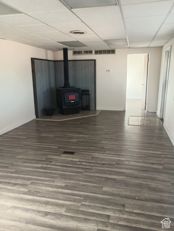 Unfurnished living room featuring a drop ceiling, wood finished floors, visible vents, baseboards, and a wood stove