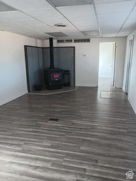 Unfurnished living room featuring a drop ceiling, wood finished floors, visible vents, baseboards, and a wood stove