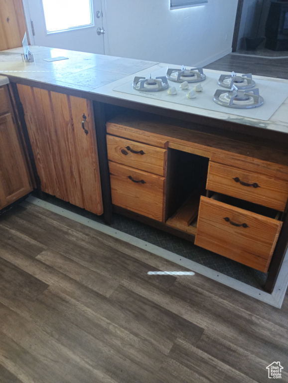 Kitchen with dark wood-style floors, white gas stovetop, tile countertops, and brown cabinets