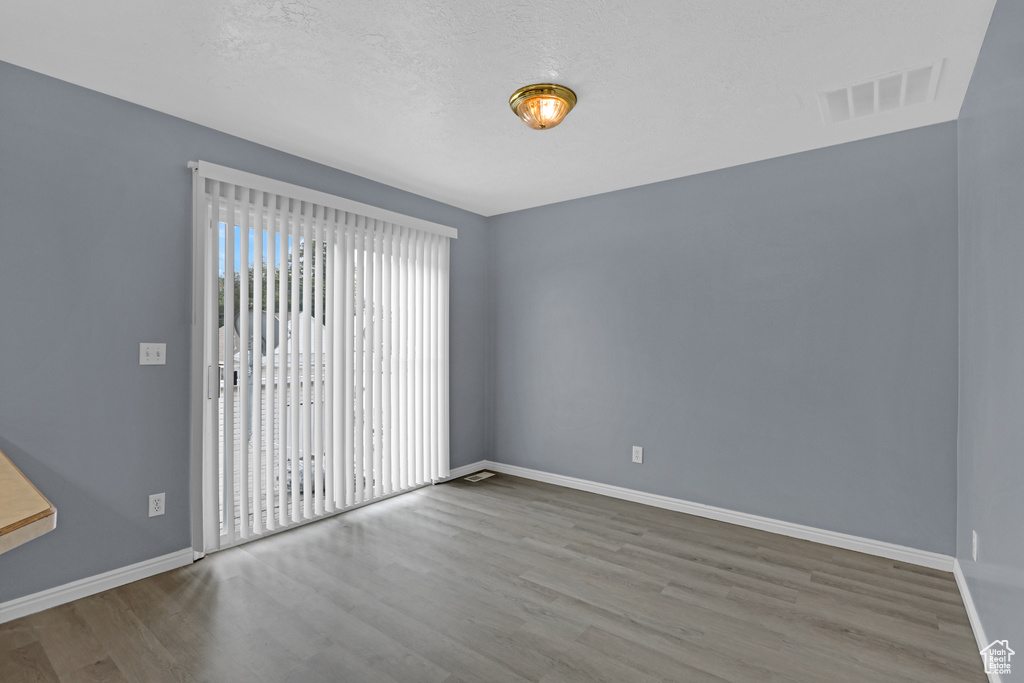 Empty room featuring a textured ceiling, wood finished floors, visible vents, and baseboards