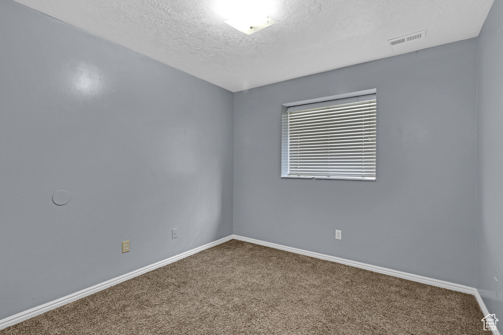 Carpeted spare room featuring baseboards, visible vents, and a textured ceiling