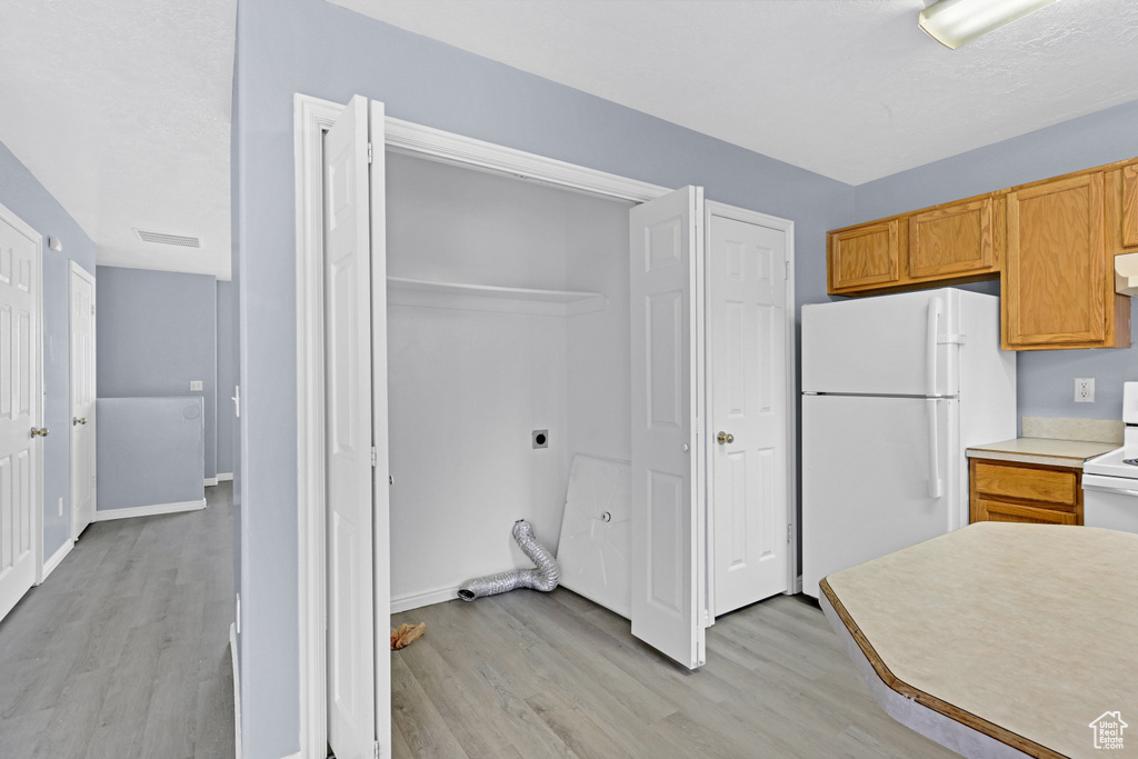 Kitchen with light countertops, visible vents, light wood-style floors, freestanding refrigerator, and ventilation hood