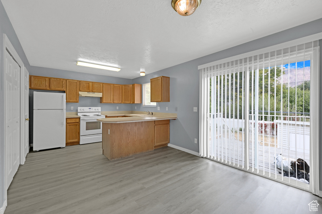 Kitchen featuring under cabinet range hood, a peninsula, white appliances, light countertops, and light wood-type flooring