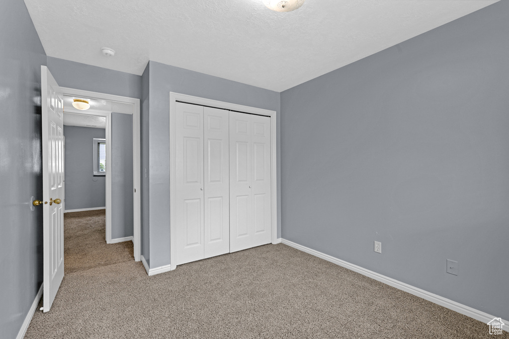 Unfurnished bedroom with a textured ceiling, a closet, baseboards, and carpet flooring