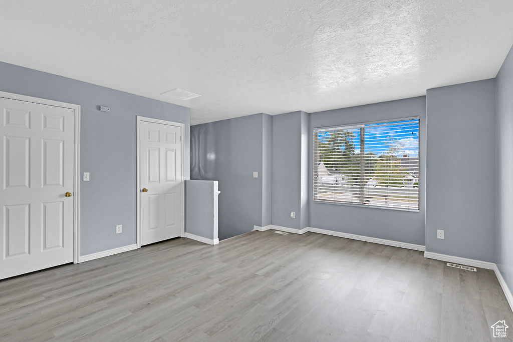 Interior space with light wood finished floors, visible vents, baseboards, and a textured ceiling