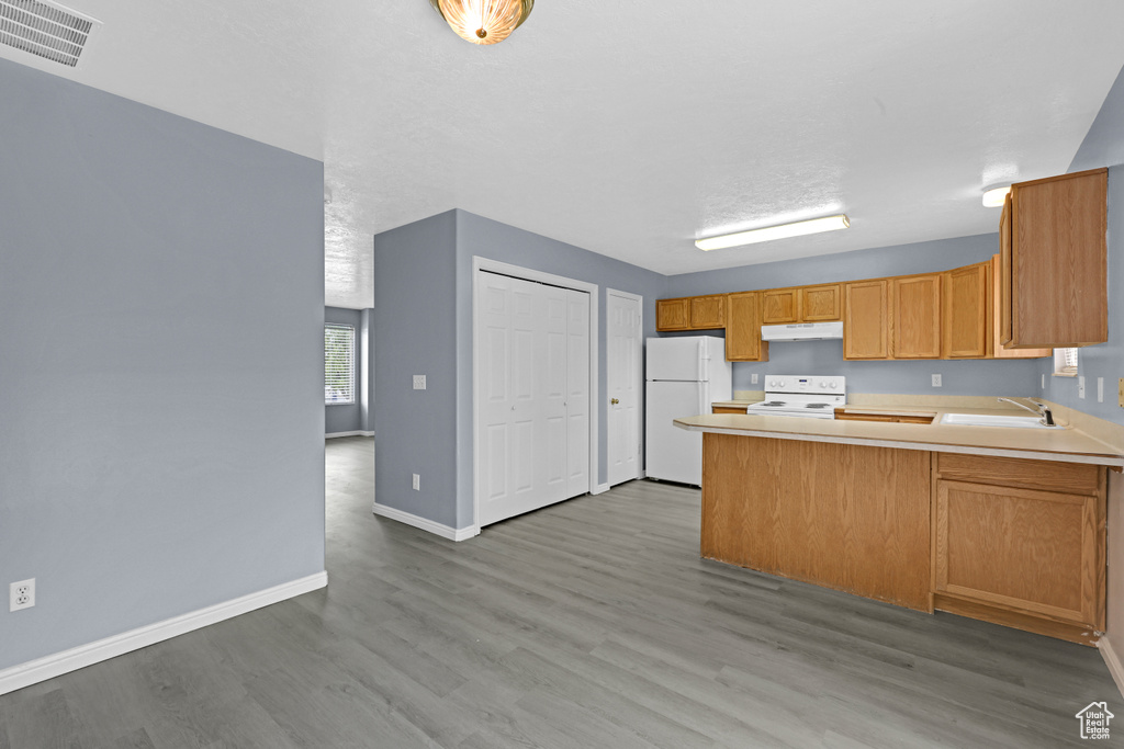 Kitchen featuring visible vents, light countertops, a peninsula, white appliances, and under cabinet range hood