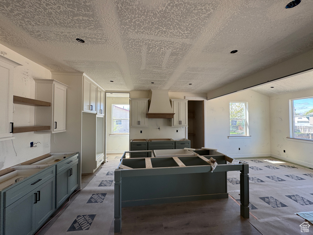 Kitchen featuring custom range hood, a center island, a textured ceiling, baseboards, and gray cabinetry