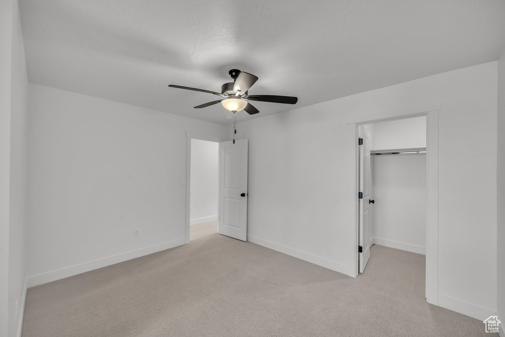 Unfurnished bedroom featuring a walk in closet, a closet, light colored carpet, ceiling fan, and baseboards