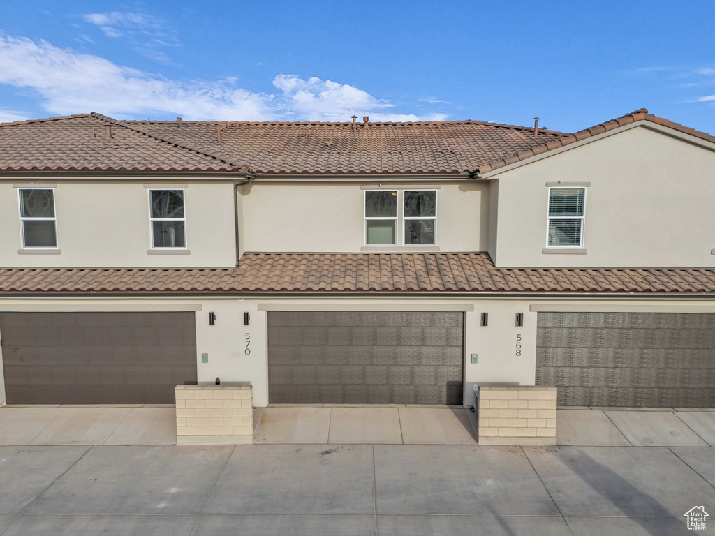 View of property with concrete driveway, a tiled roof, and stucco siding