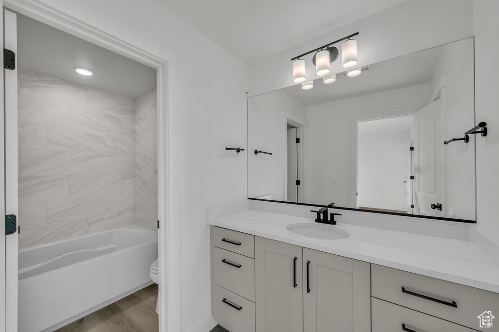 Bathroom with toilet, shower / bathing tub combination, wood finished floors, and vanity