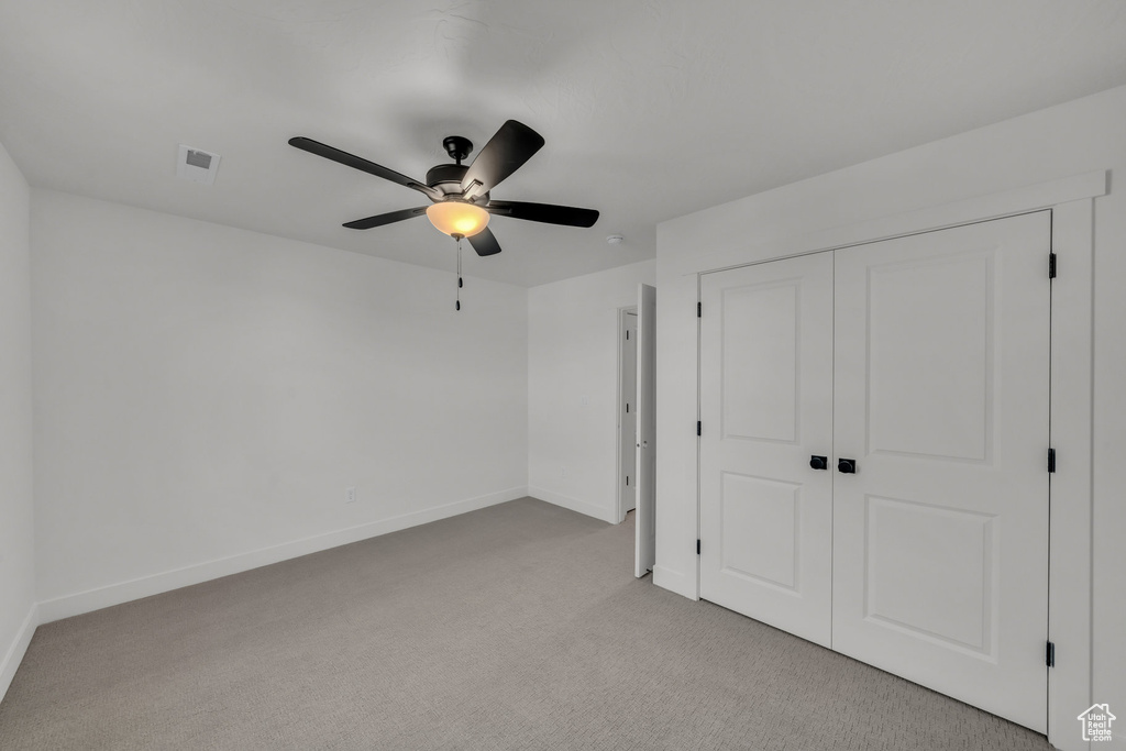 Unfurnished bedroom with light carpet, visible vents, baseboards, ceiling fan, and a closet