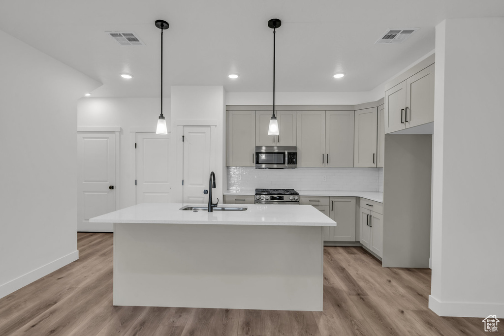Kitchen with stainless steel appliances, a sink, visible vents, light wood-type flooring, and tasteful backsplash