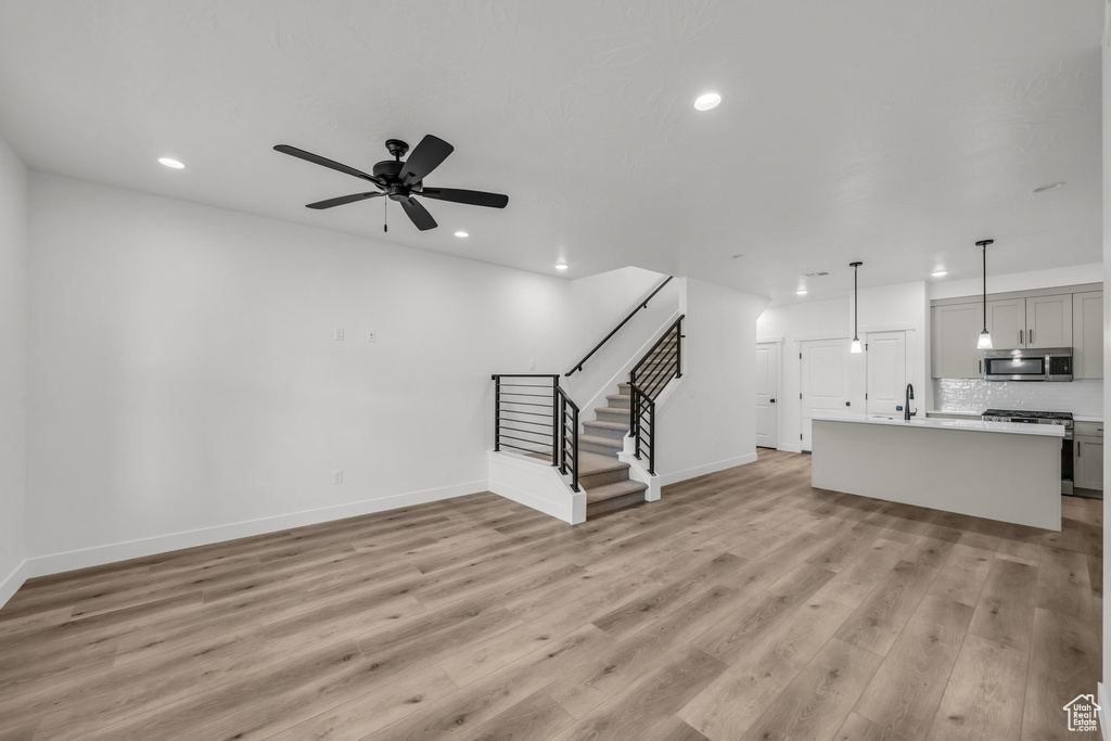 Unfurnished living room with recessed lighting, a ceiling fan, light wood-type flooring, baseboards, and stairs