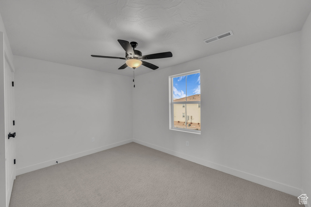 Empty room with baseboards, ceiling fan, visible vents, and light colored carpet