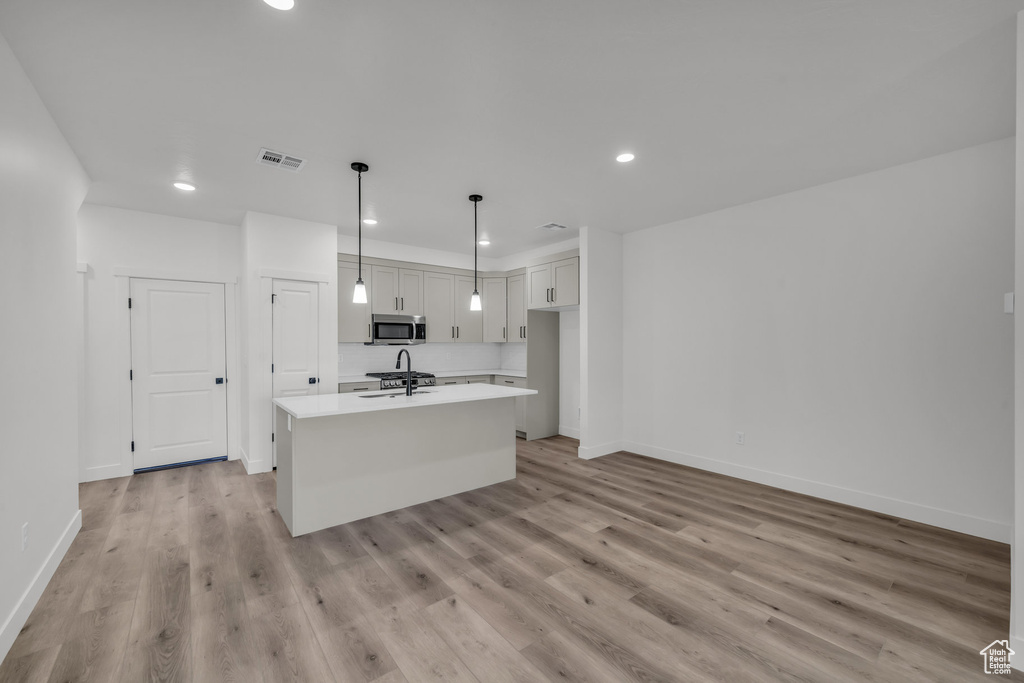 Kitchen featuring light countertops, stainless steel microwave, visible vents, light wood-style floors, and an island with sink