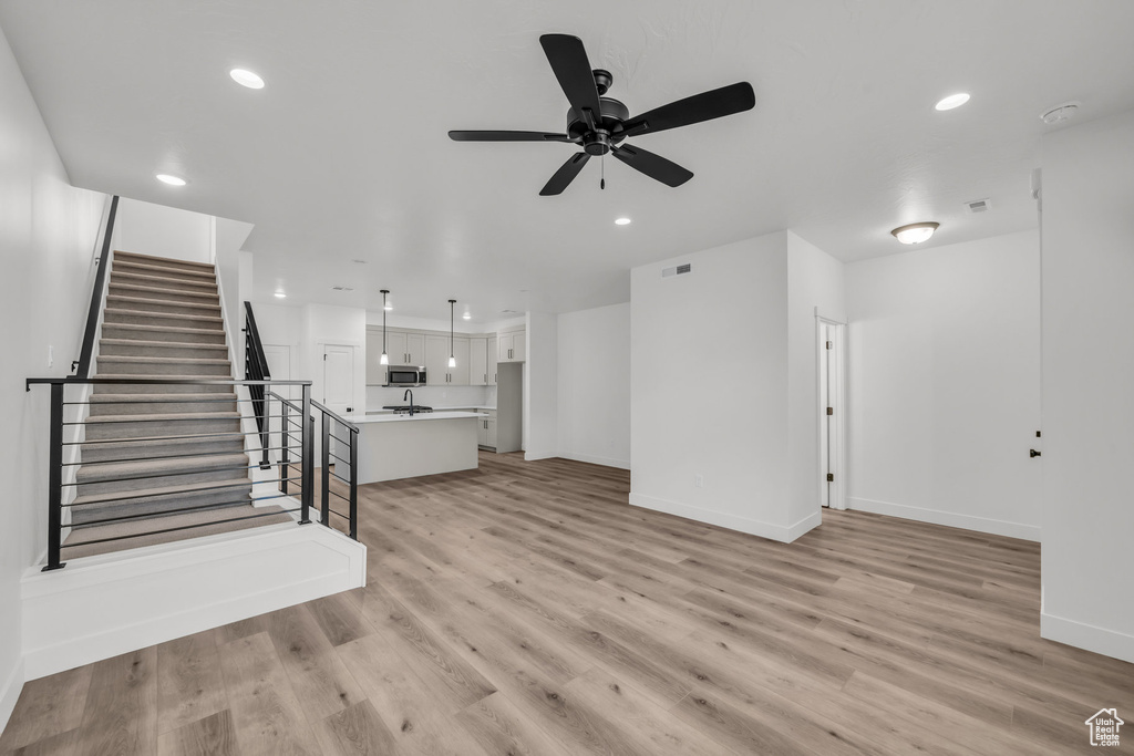 Unfurnished living room featuring recessed lighting, visible vents, baseboards, light wood-style floors, and stairway