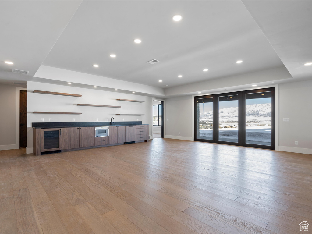 Unfurnished living room with wine cooler, a tray ceiling, indoor wet bar, visible vents, and light wood-type flooring