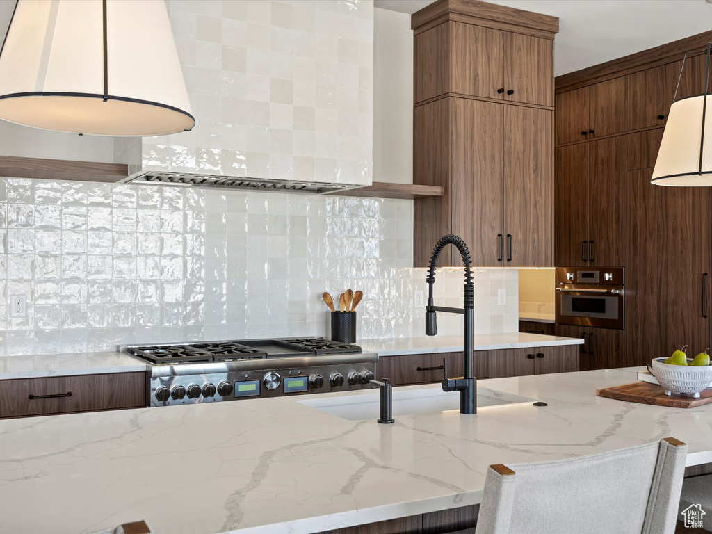 Kitchen with light stone counters, tasteful backsplash, appliances with stainless steel finishes, a sink, and wall chimney exhaust hood