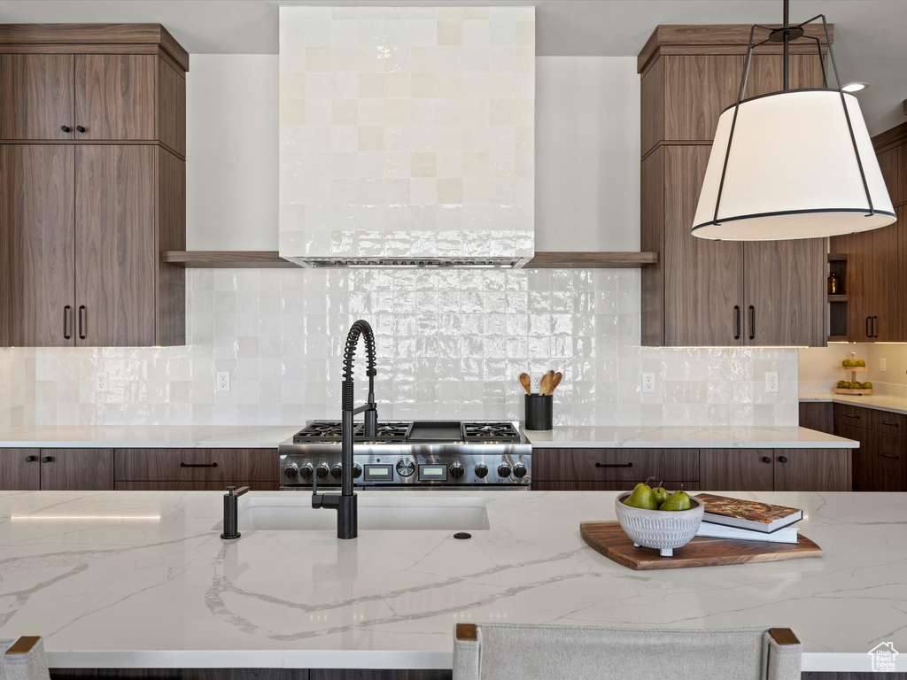 Kitchen with open shelves, hanging light fixtures, decorative backsplash, light stone countertops, and wall chimney exhaust hood