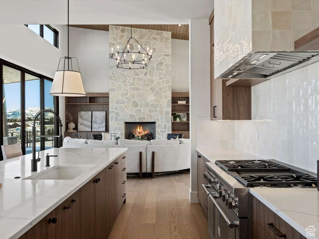 Kitchen featuring light wood finished floors, a towering ceiling, a sink, high end range, and wall chimney exhaust hood