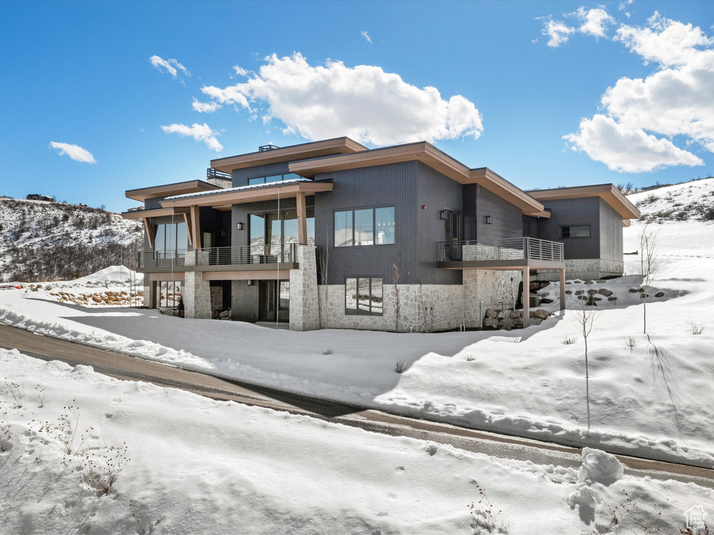 Snow covered house featuring stone siding and a balcony